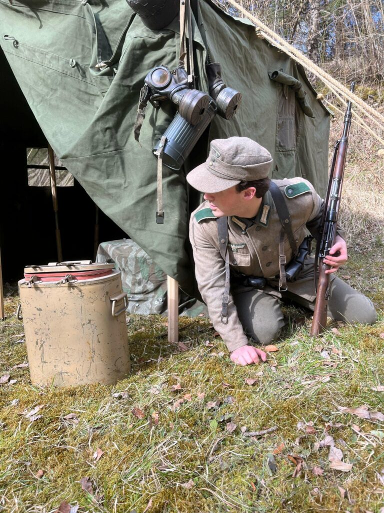 Reconstitution d’un allemand en tenue historique devant une tente militaire, fusil à la main pour le tournage du film "Eclaireur"